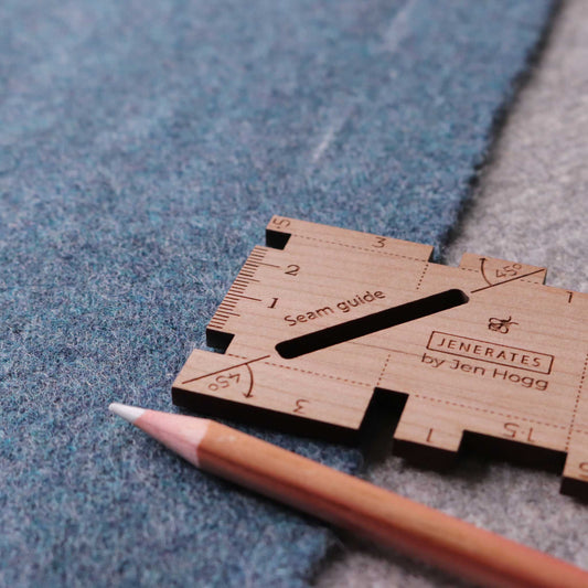 A wooden sewing seam guide sitting on some gray-blue felt and a wooden colored pencil