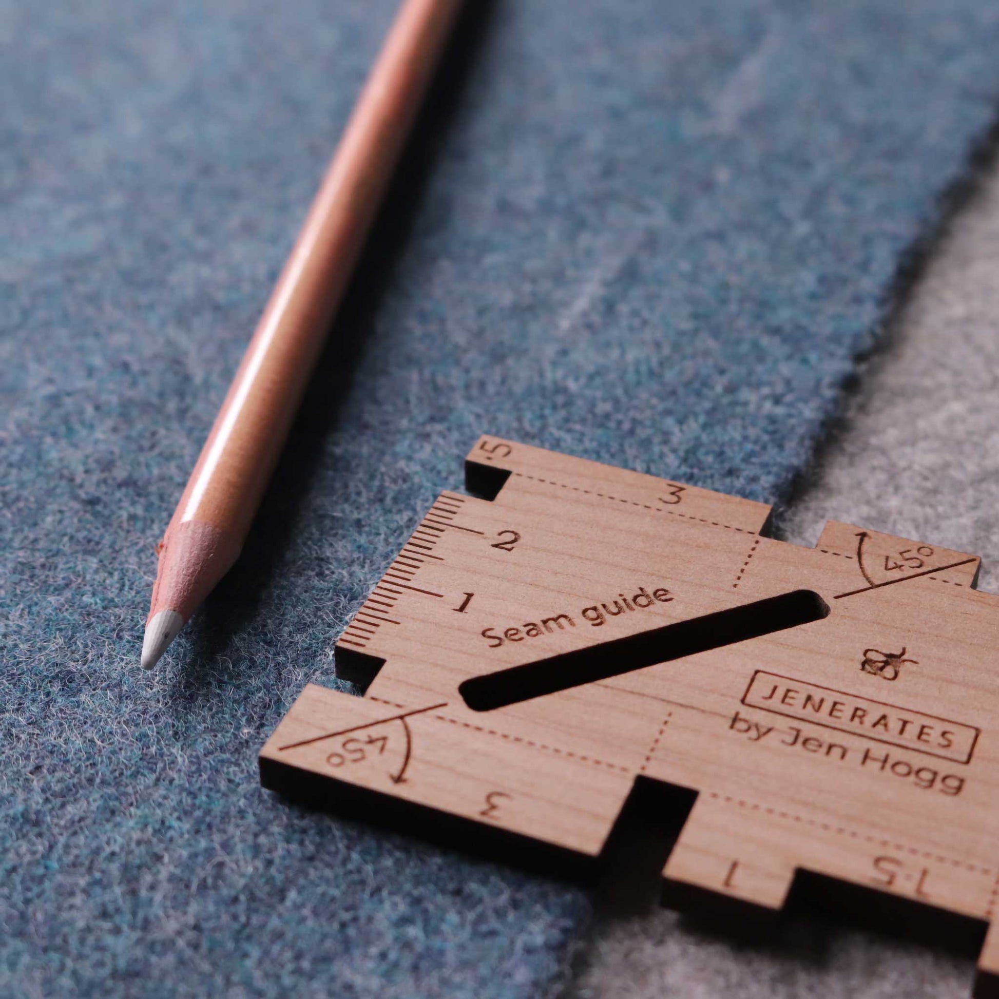 A wooden sewing seam guide sitting on some gray-blue felt and a wooden colored pencil