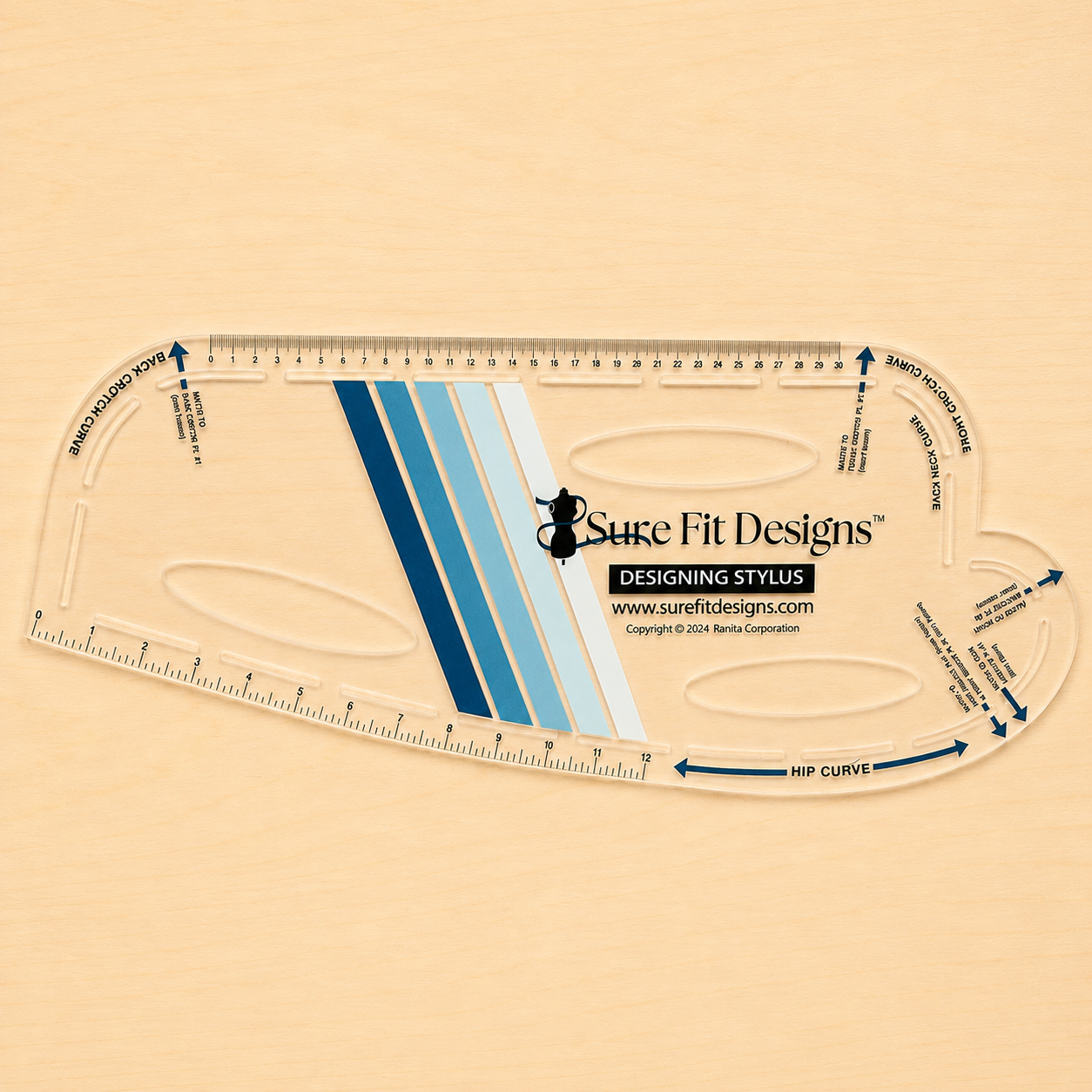 A clear high grade plastic measuring tool labeled Sure Fit Designs Designing Stylus, shown on a light beige wood background. The tool includes printed measurement markings, blue and white diagonal stripes, and printed guide text and arrows.