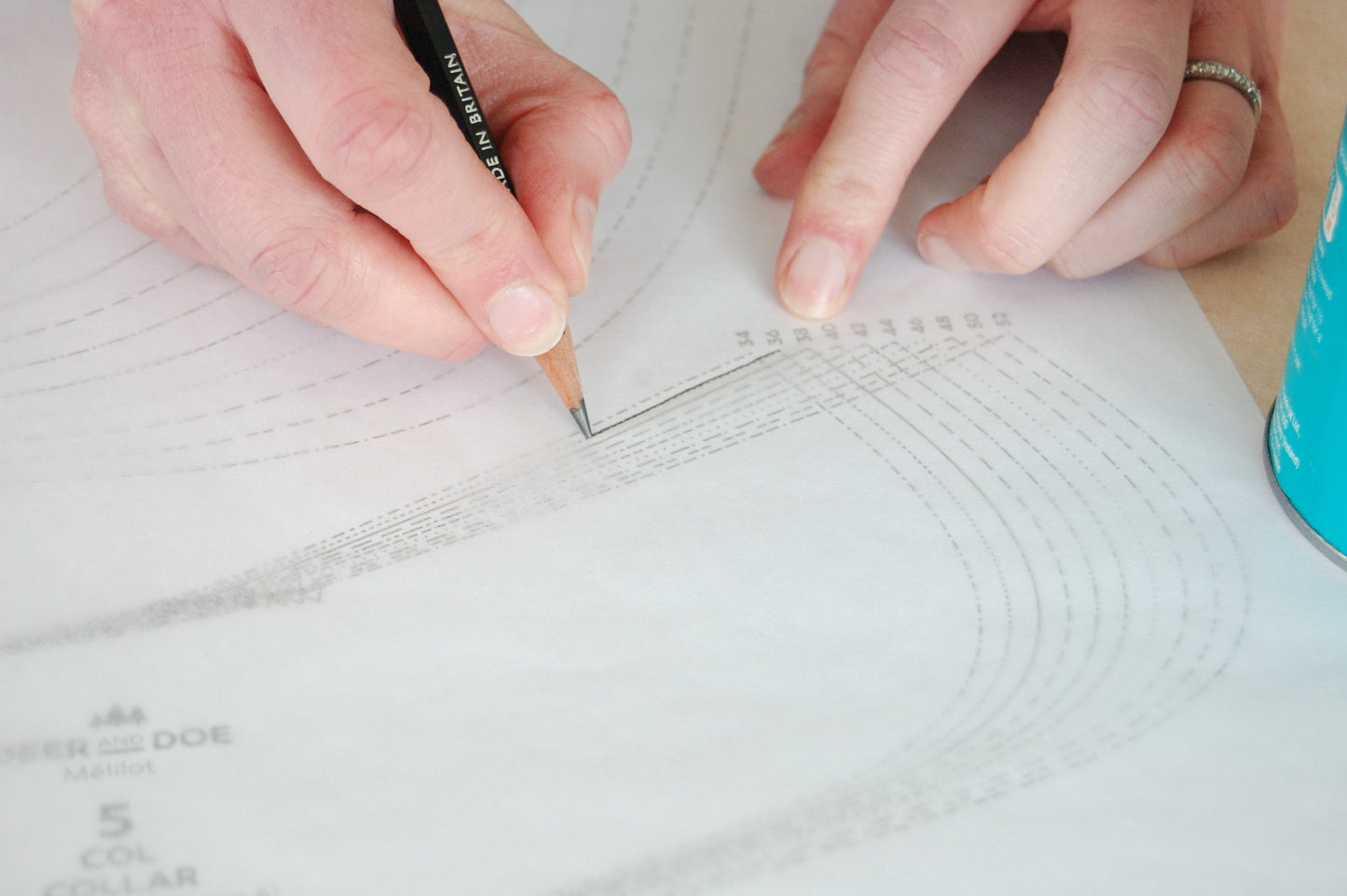 A picture of Patterntrace tracing paper over a pattern and two hands drawing with a black pencil