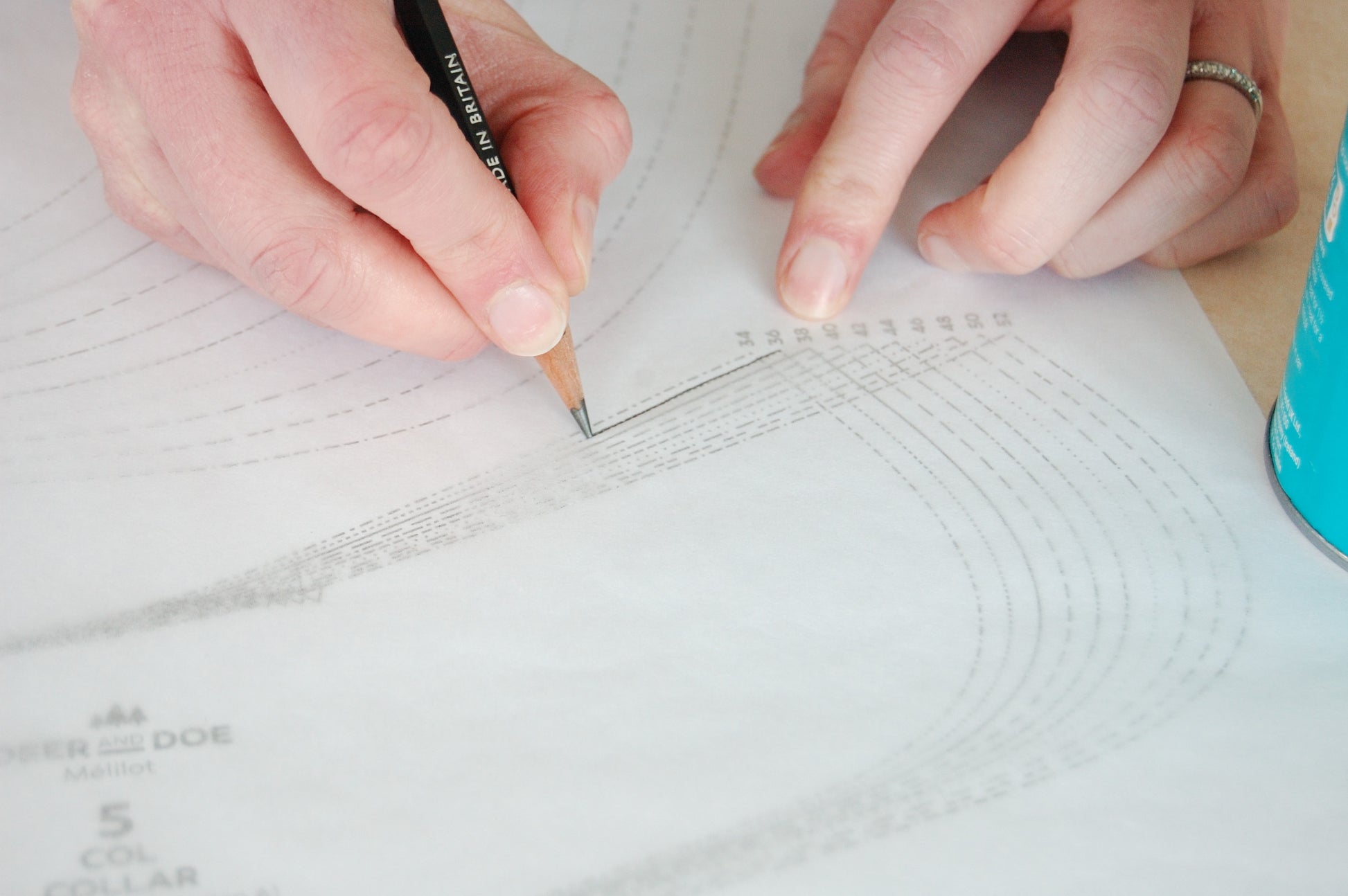 A picture of Patterntrace tracing paper over a pattern and two hands drawing with a black pencil