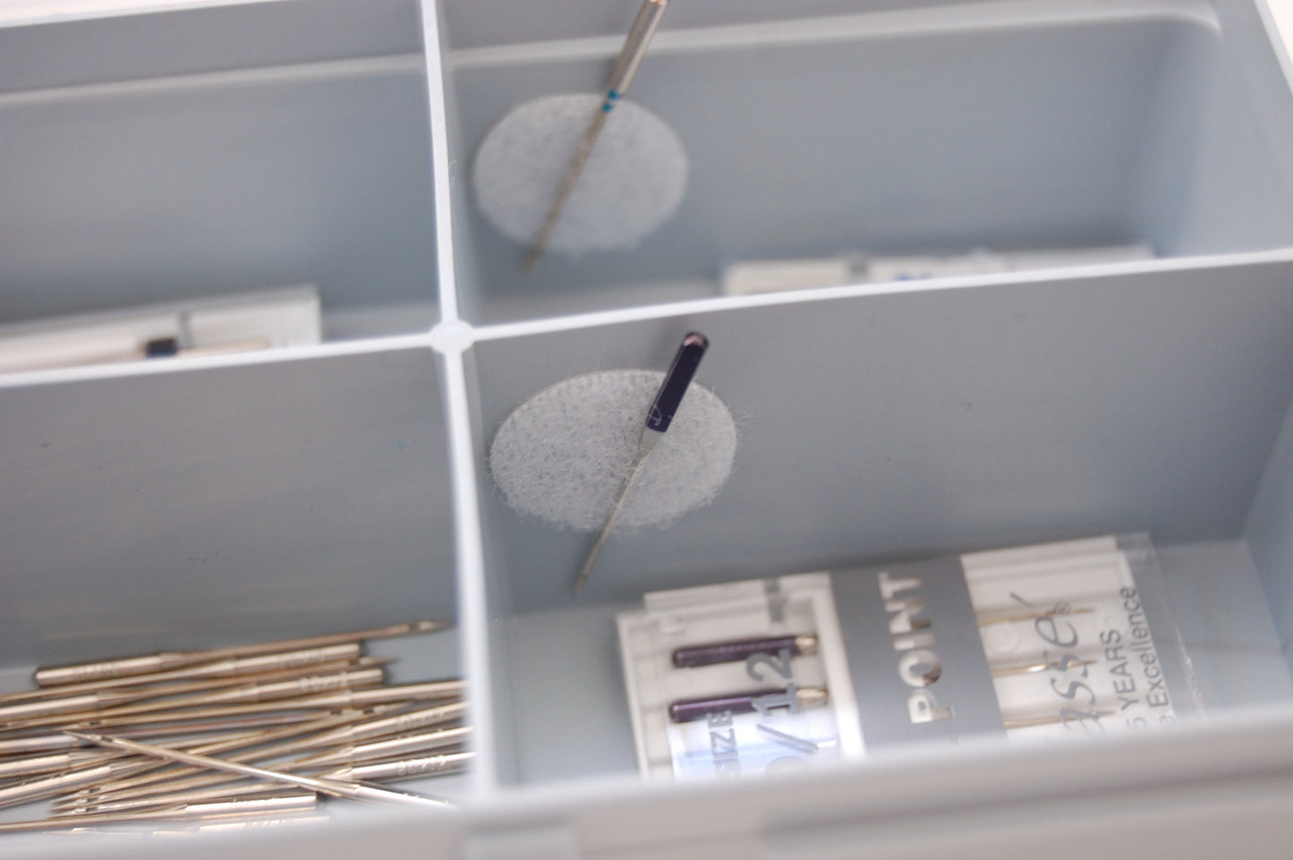 An up close view of the compartments in the needle store. There is a circle of white velco and sewing needles being stored in the velcro