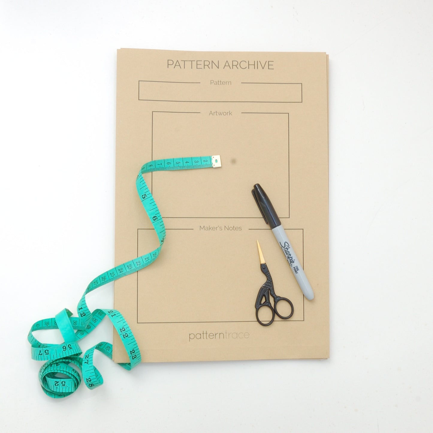 a large paper bag colored Pattern Archive envelopes from Patterntrace that has a teal measuring tape and bird shaped scissors and a black sharpie marker on the bottom of the photo