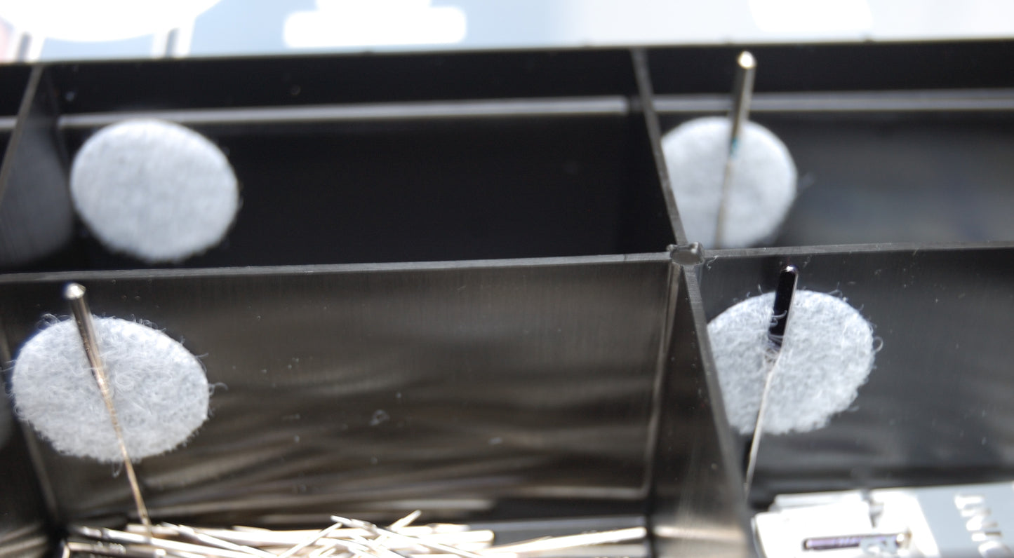 An up close view of the compartments in the needle store. There is a circle of white velco and sewing needles being stored in the velcro