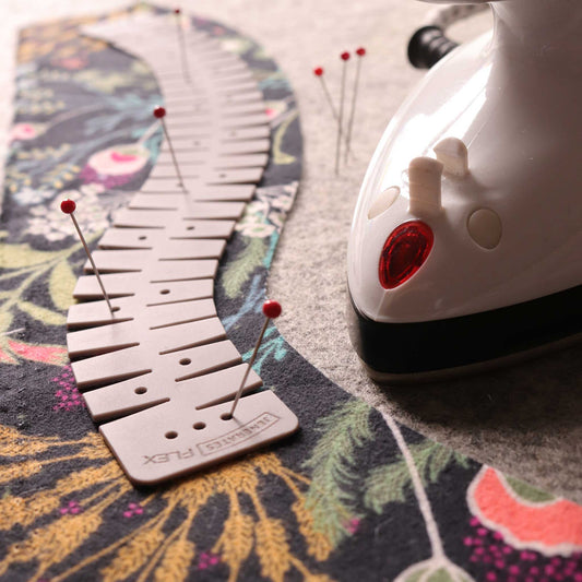 a tan flexible silicone hemmer on some floral fabric with a mini iron sitting on a gray wool mat