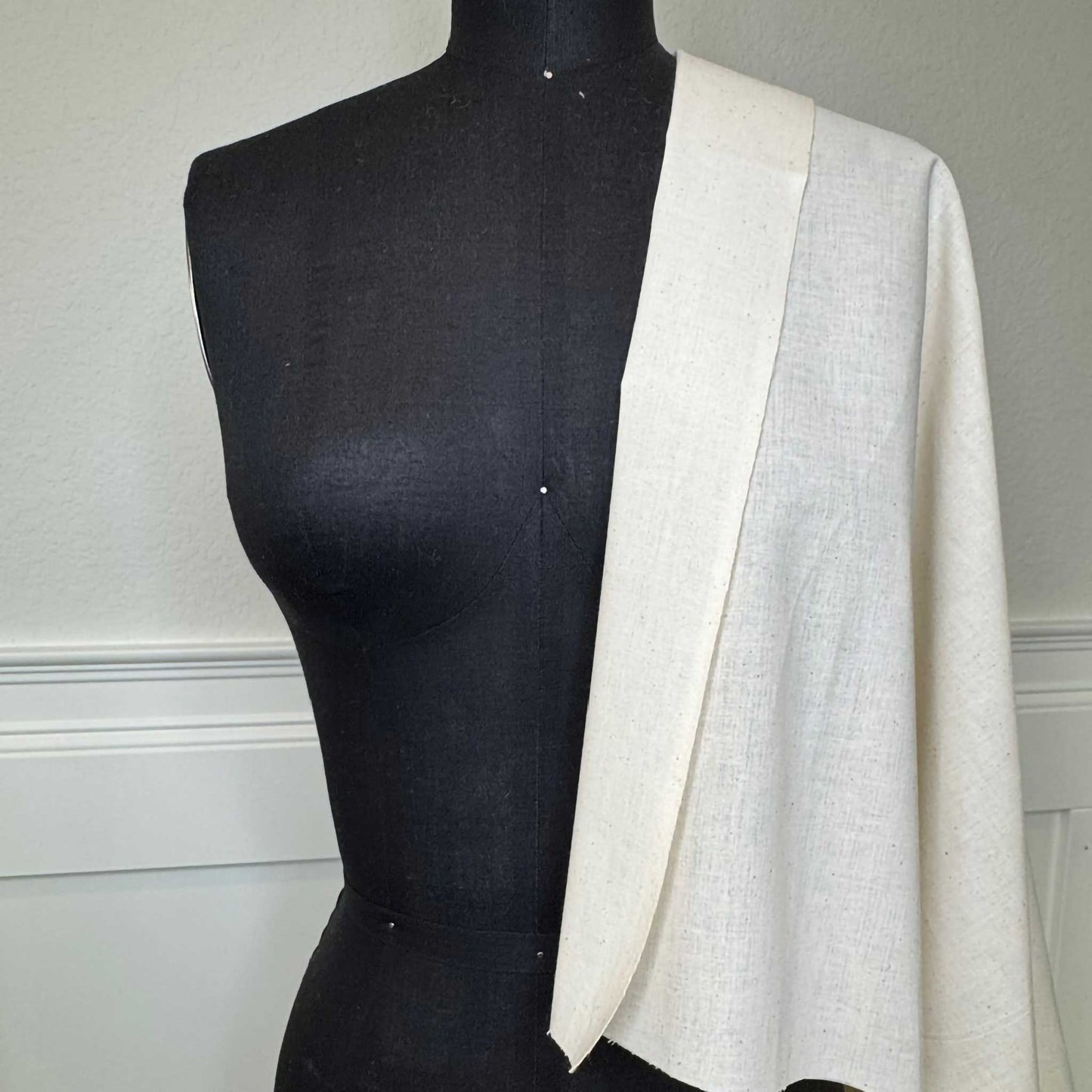 A black female mannequin torso with beige muslin fabric draped over the shoulder on the right