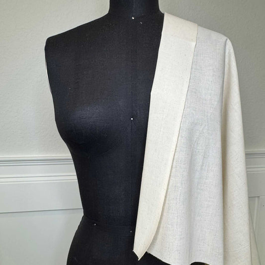 A black female mannequin torso with beige muslin fabric draped over the shoulder on the right
