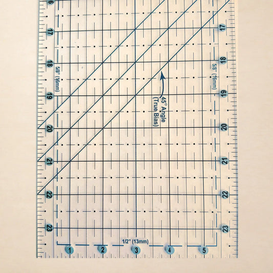 A clear quilting ruler with blue printed grid lines, measurement markings, and diagonal guide lines, shown on a light beige background.
