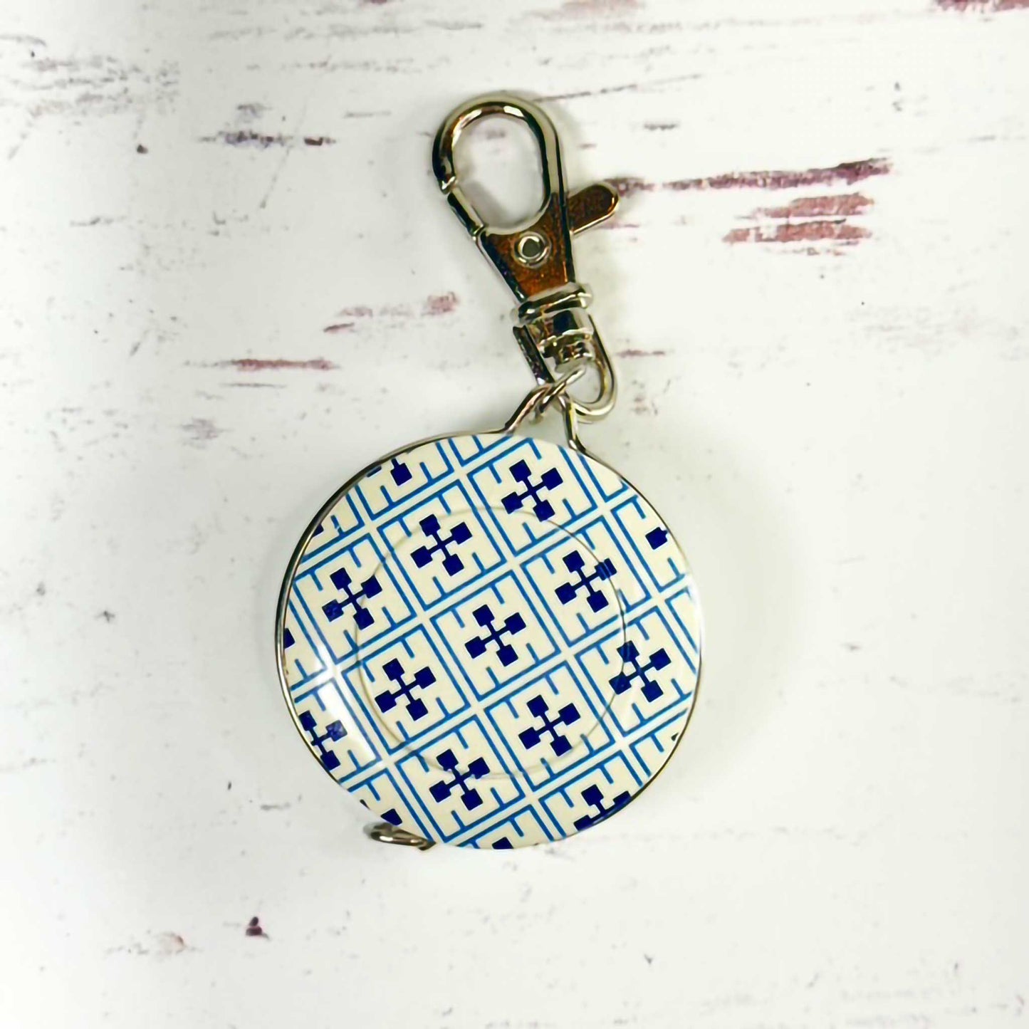 blue and white circular tape measure/keychain with a metal clasp on a textured white background