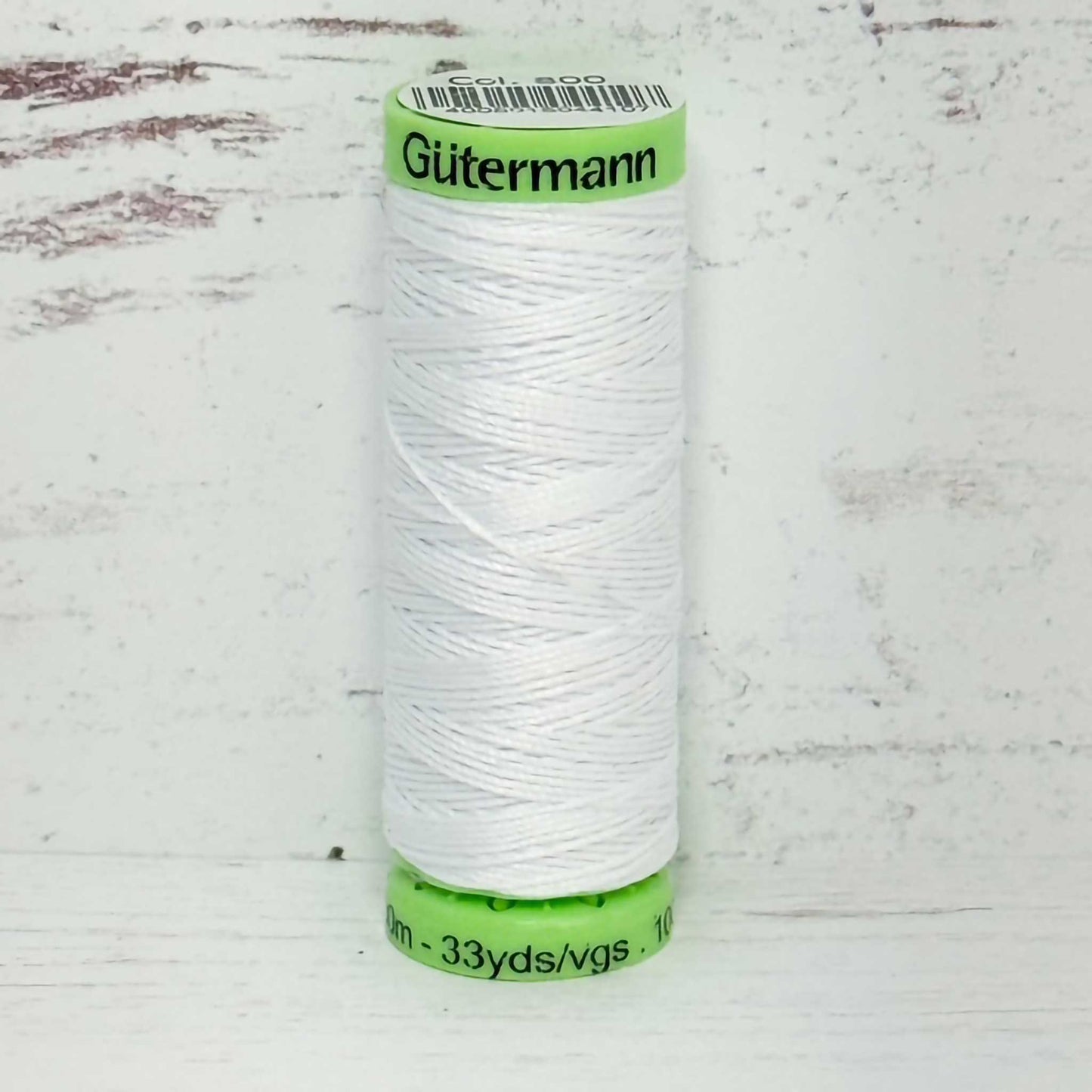 Spool of white top stitch thread with a green label on a light wooden background