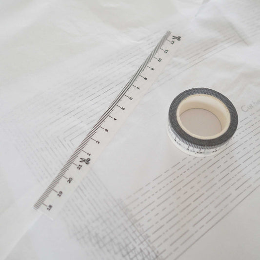 a spool of washi tape viewed from the top and a strip of tape diagonally above it.  The tape is white with black ink measuring centimeters