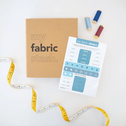A brown paper bag colored book that says "my fabric stash" and a page of stickers that are shades of blue on a white background that describe the  seasons and occasions to wear clothing.  There is a yellow and white tape measure on the lower left corner and red and blue spools of thread in the upper right corner