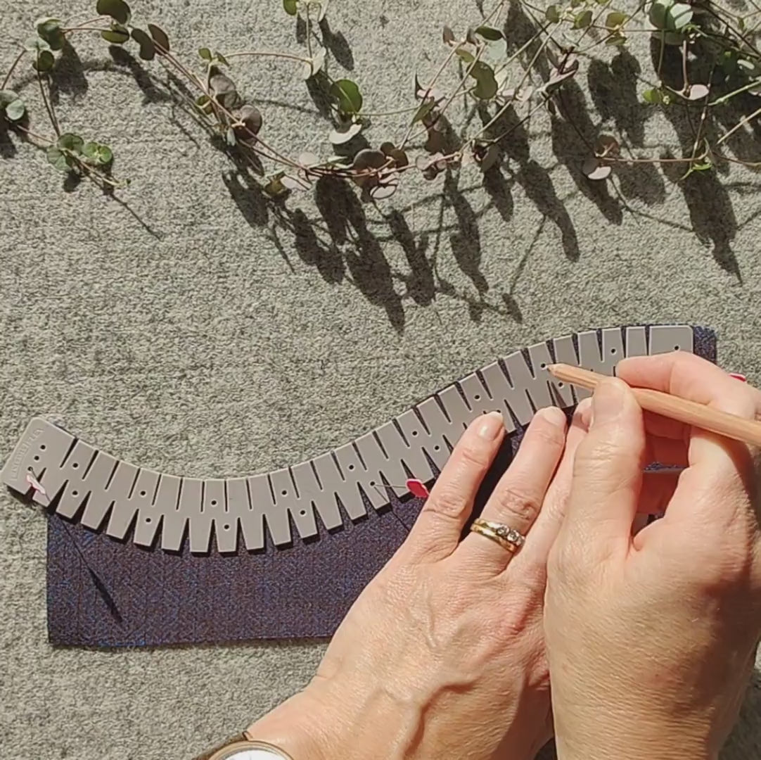 A gray silicone flexible hemmer with plum colored fabric and some hands demonstrating how to use the hemmer
