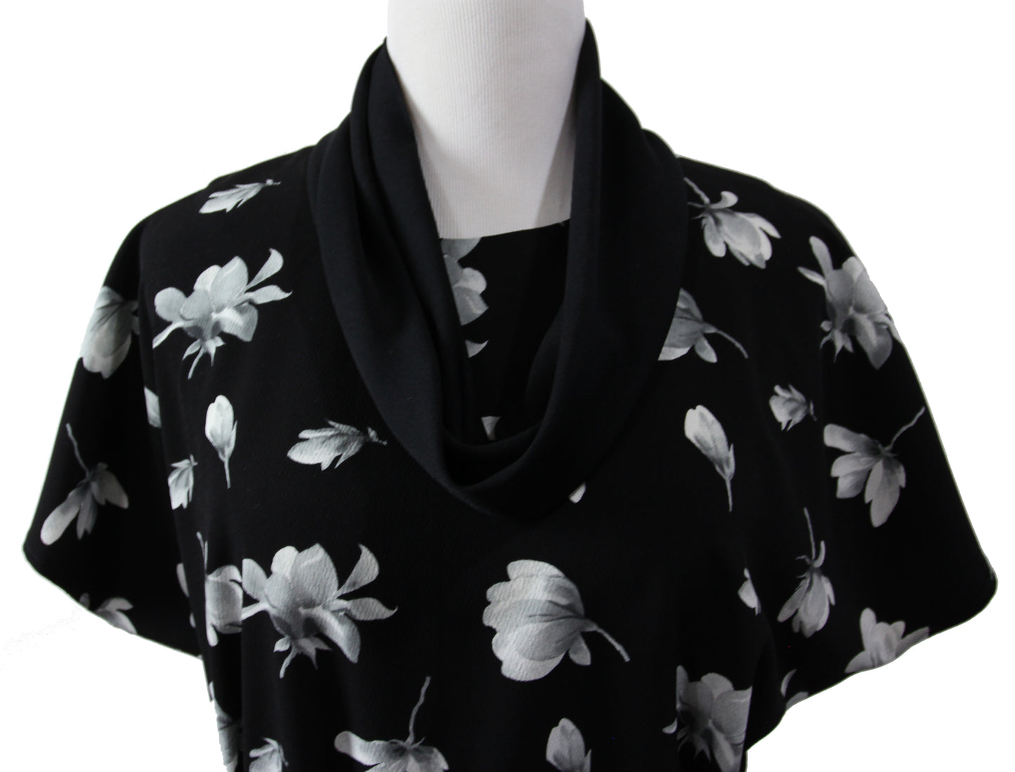 A close up of a short sleeve blouse on a mannequin. it is made of black fabric with large white and gray flowers and a black infinity scarf