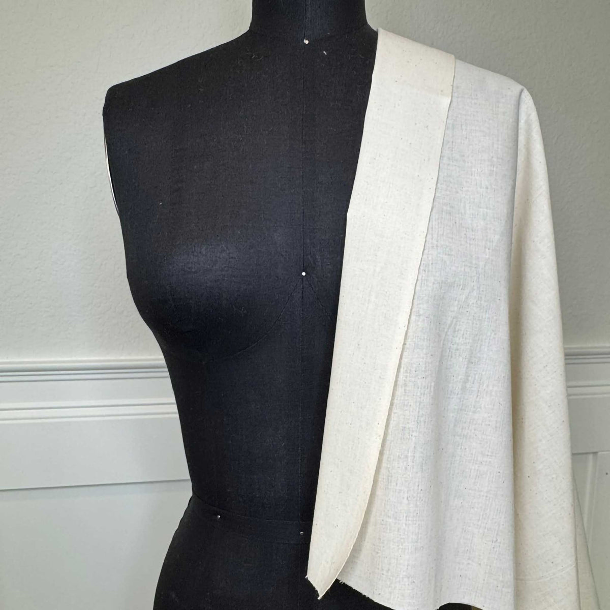 A black female mannequin with some muslin fabric draped on the shoulder