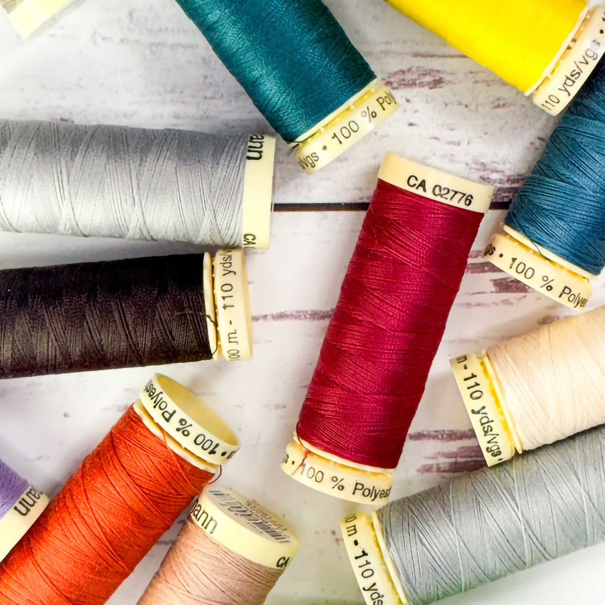 spools of colorful Gutermann thread scattered on a white wood surface