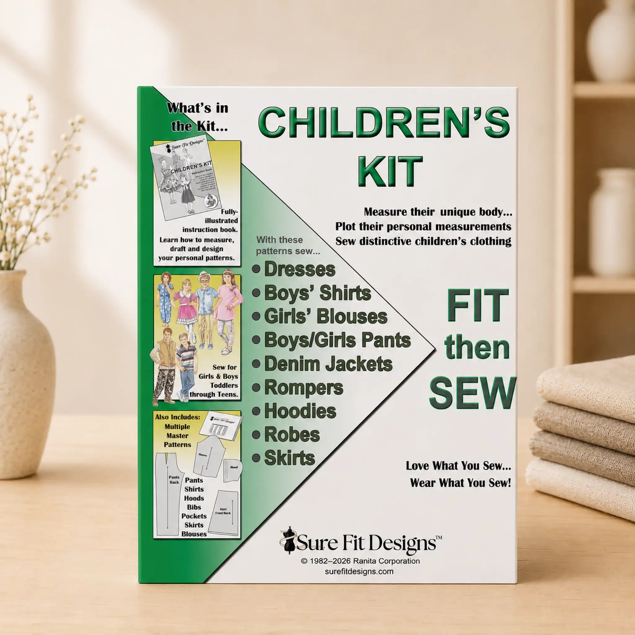 A sewing kit box for children's clothing by Sure Fit Designs, standing upright on a wooden surface with a soft-focus warm indoor background. The box is white and green with large text reading 'CHILDREN'S KIT' and 'FIT then SEW', plus a list of garment types and a small product photo panel on the left.