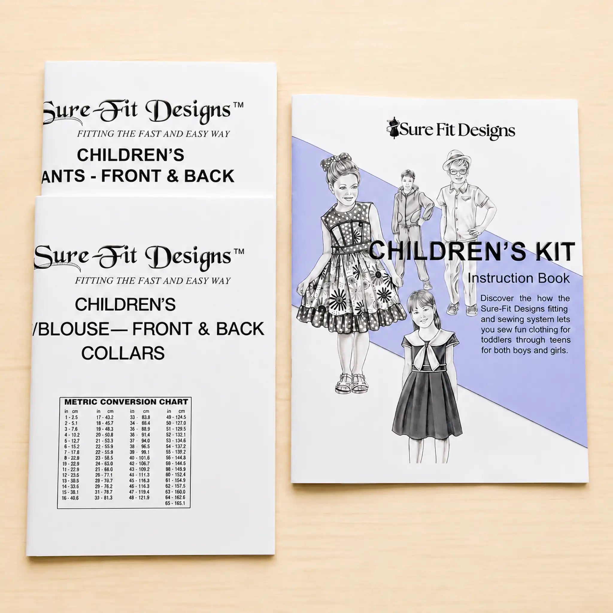 Two printed sewing pattern booklets from Sure Fit Designs laid on a light wood surface. One booklet shows children's pants front and back, and the other shows a children's kit instruction book cover with sewing illustrations and text.
