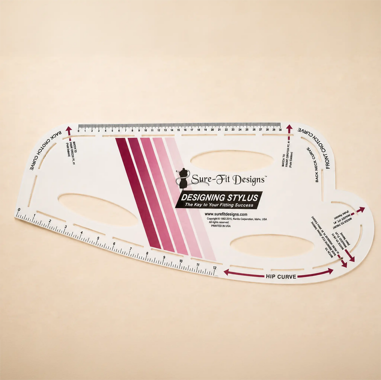 A Sure-Fit Designs Designing Stylus hip curve and back curve measurer, shown on a warm beige background. The clear plastic tool features printed measurement guides, black text, and a pink and purple striped brand graphic.