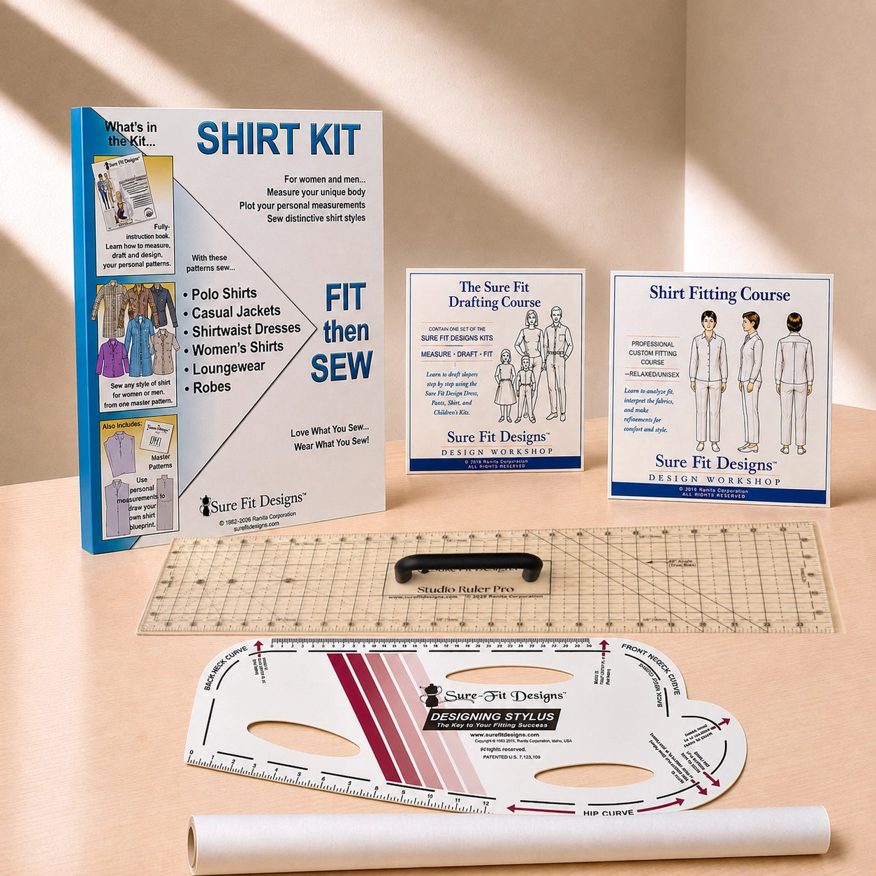 Sure Fit Designers shirt fitting kit displayed on a beige surface with warm sunlight shadows. The kit includes a main instruction booklet, three smaller course/booklet covers, a clear gridded cutting mat, a white arched template, and a white roll of paper.