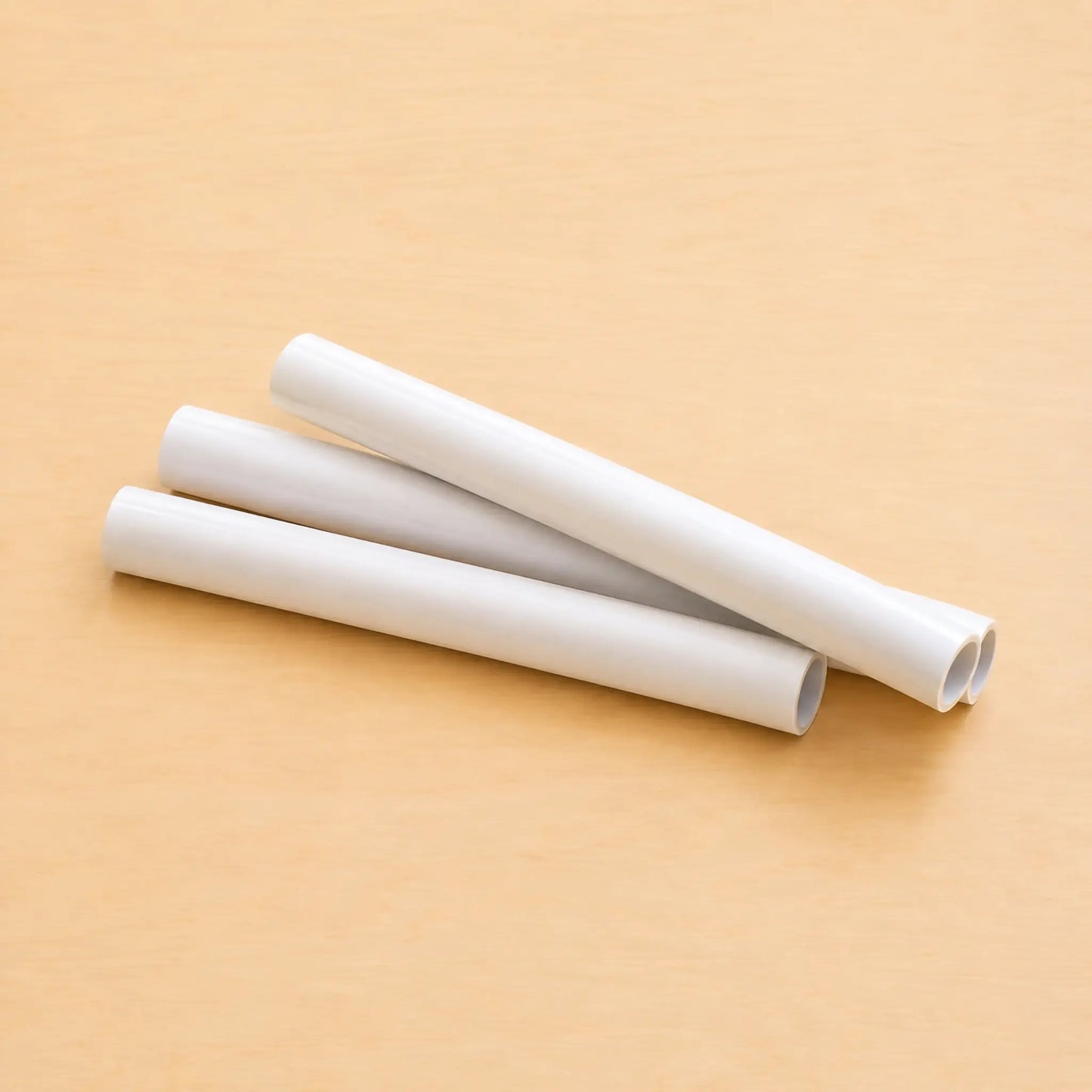 Three white rolls of Hahnemühle transparent tracing paper arranged diagonally on a light maple table.