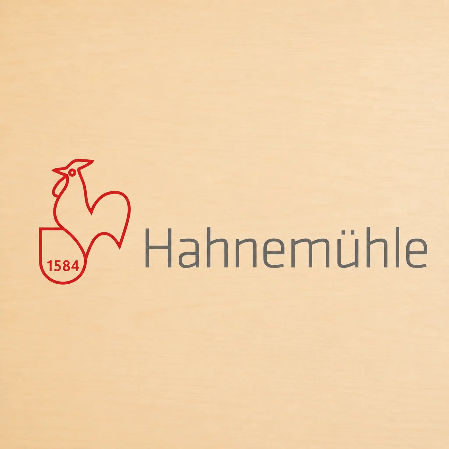 A close-up of a light beige wood surface featuring a red rooster outline logo with the number 1584 and the word Hahnemühlä in dark gray text.