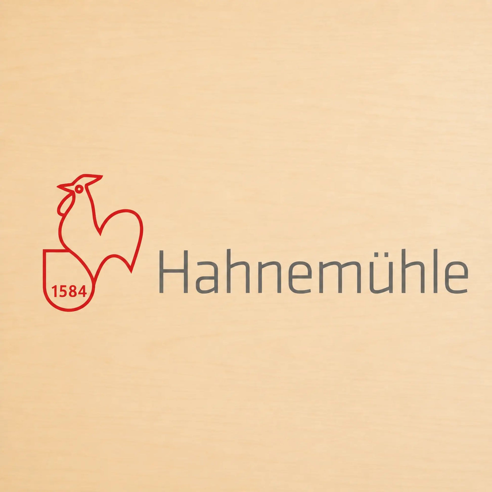 A close-up of a light beige wood surface featuring a red rooster outline logo with the number 1584 and the word Hahnemühlä in dark gray text.