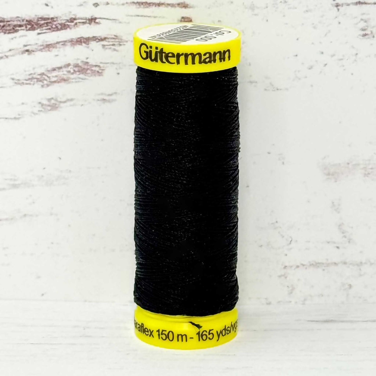 Spool of black Gutermann thread on a light gray background