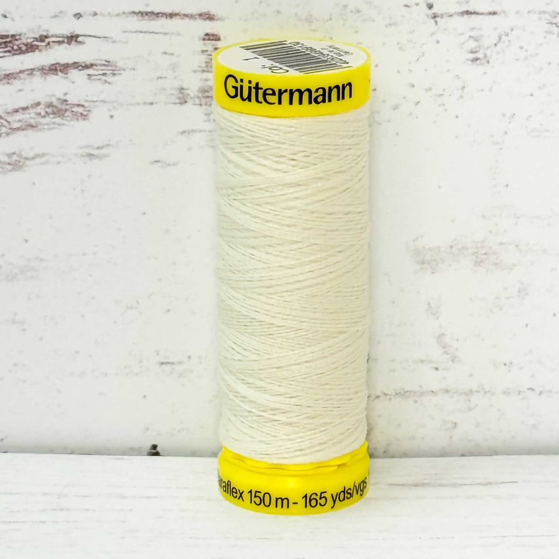 Spool of ivory Gutermann thread on a wooden surface