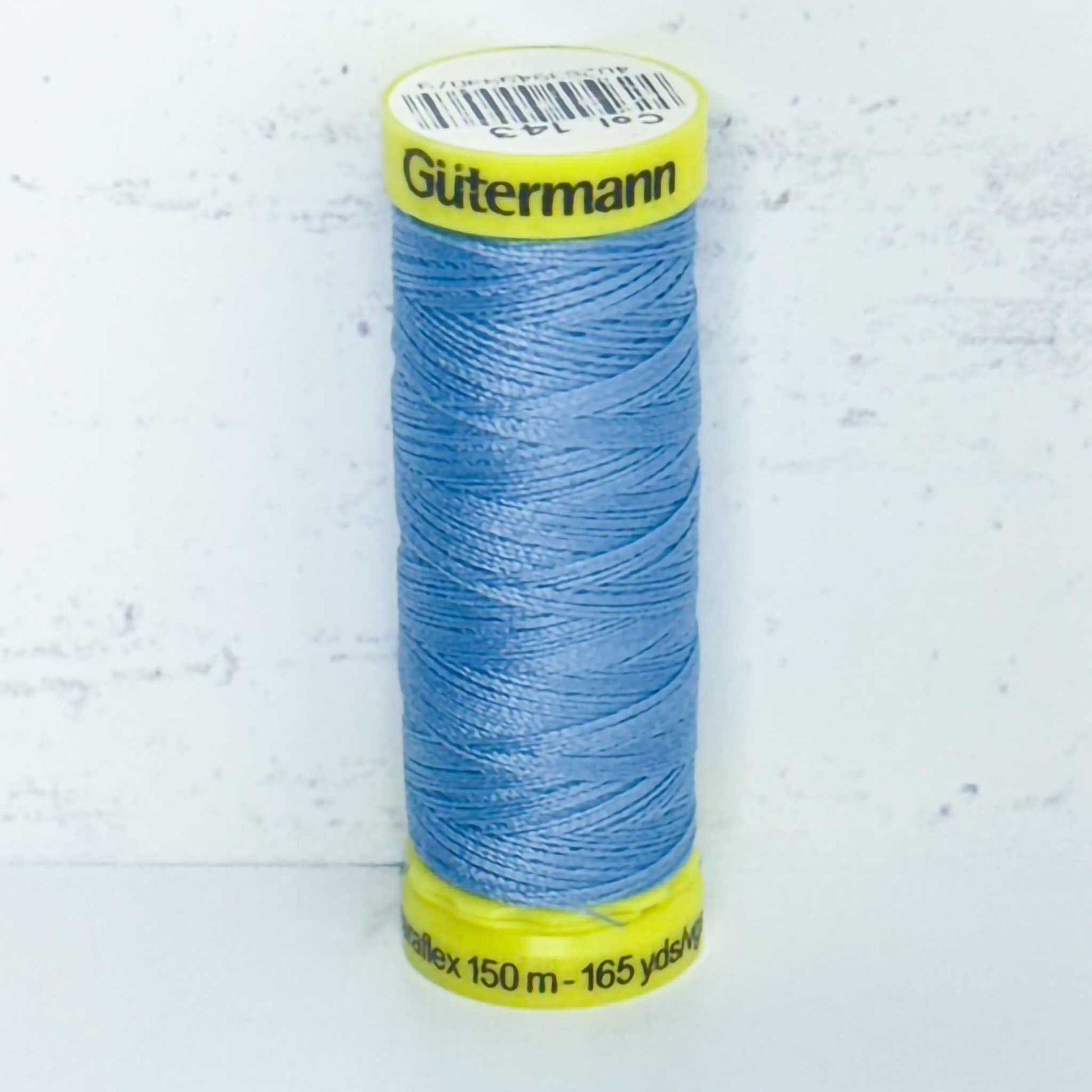 Spool of blue Gutermann thread on a light gray background