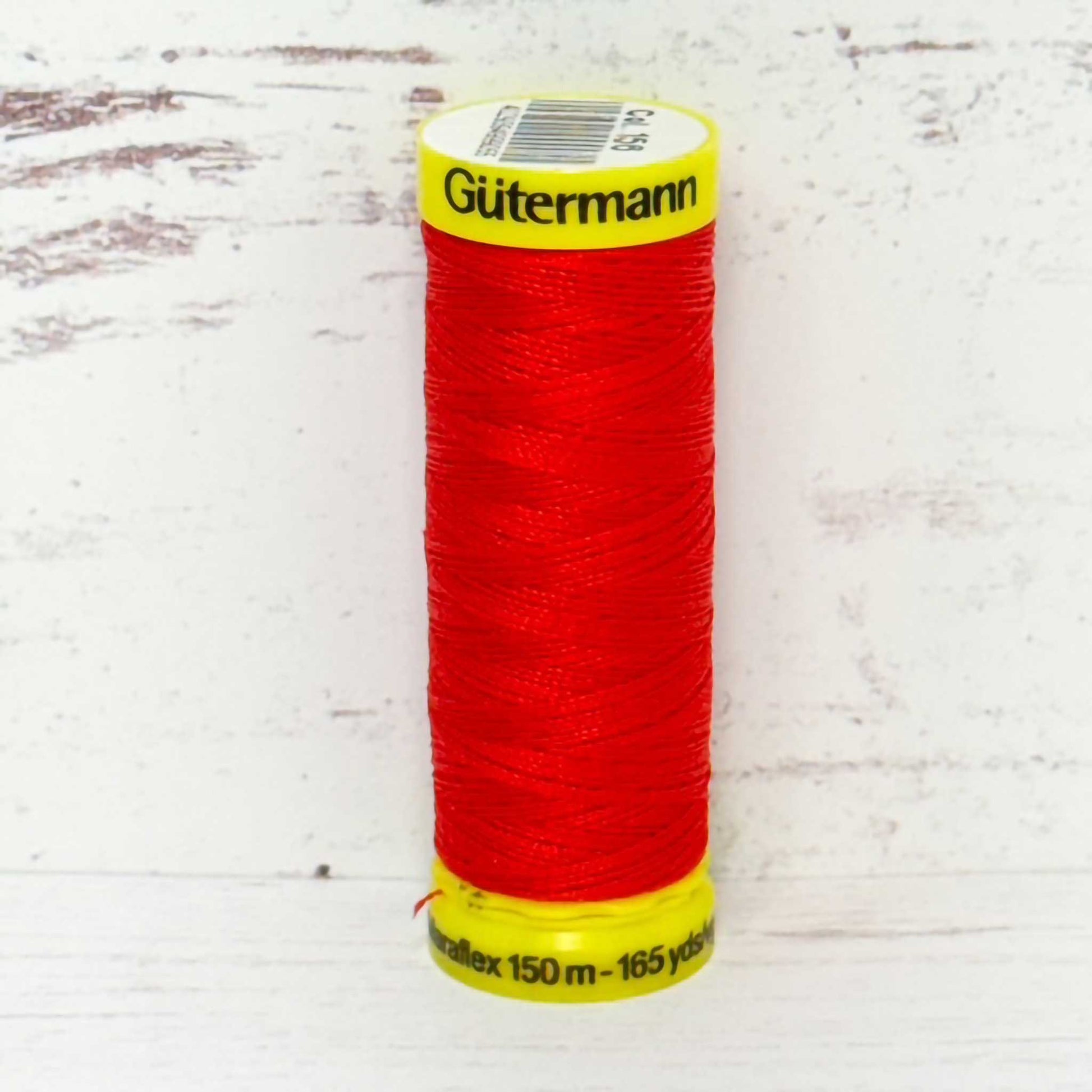 Red spool of Gutermann thread on a light wooden surface