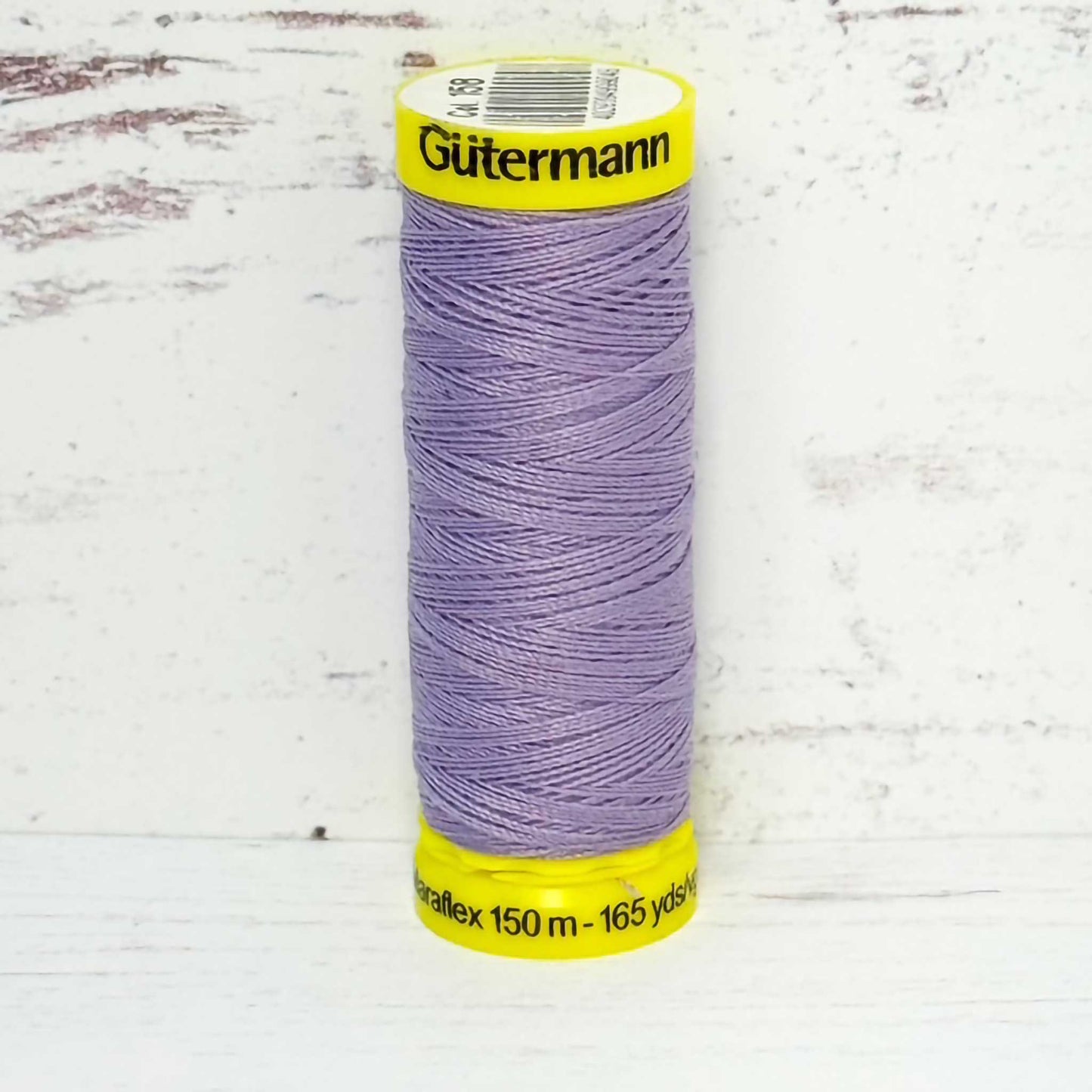 Spool of lavender Gutermann thread on a light wooden surface