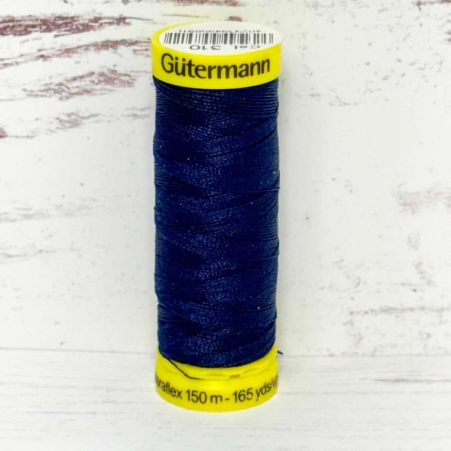 Spool of blue Gutermann thread on a light wooden background