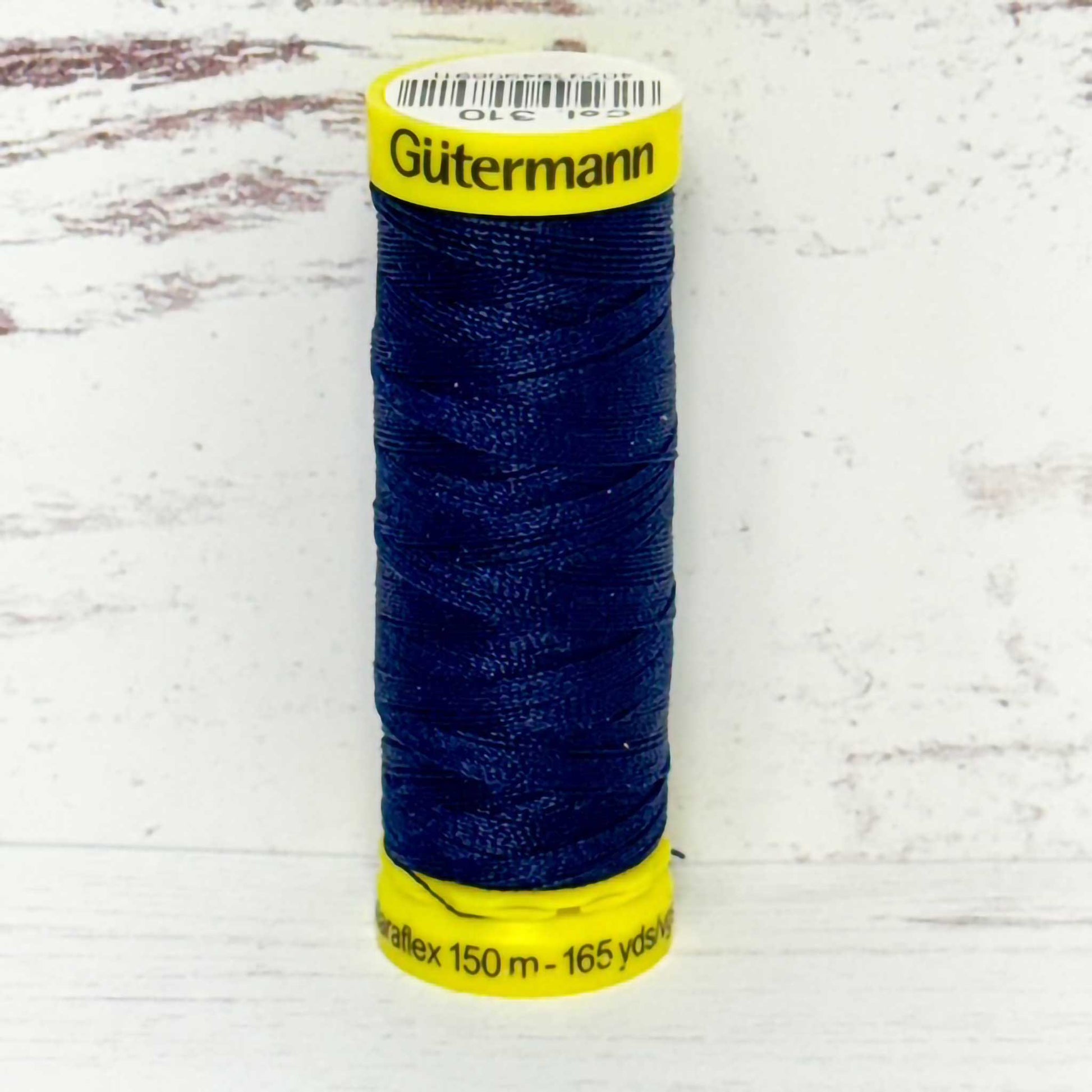 Spool of blue Gutermann thread on a light wooden background