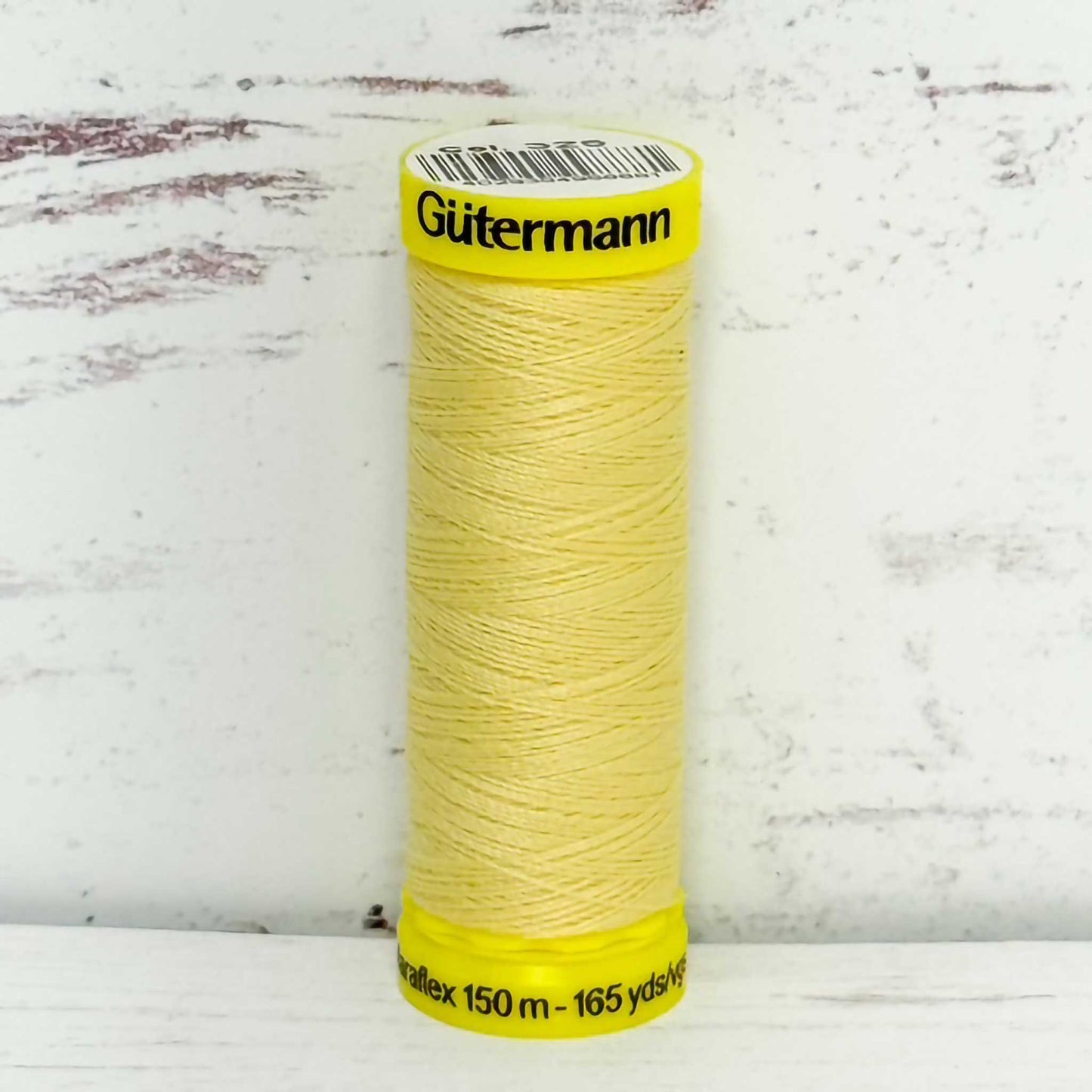 Spool of yellow Gutermann thread on a textured white background