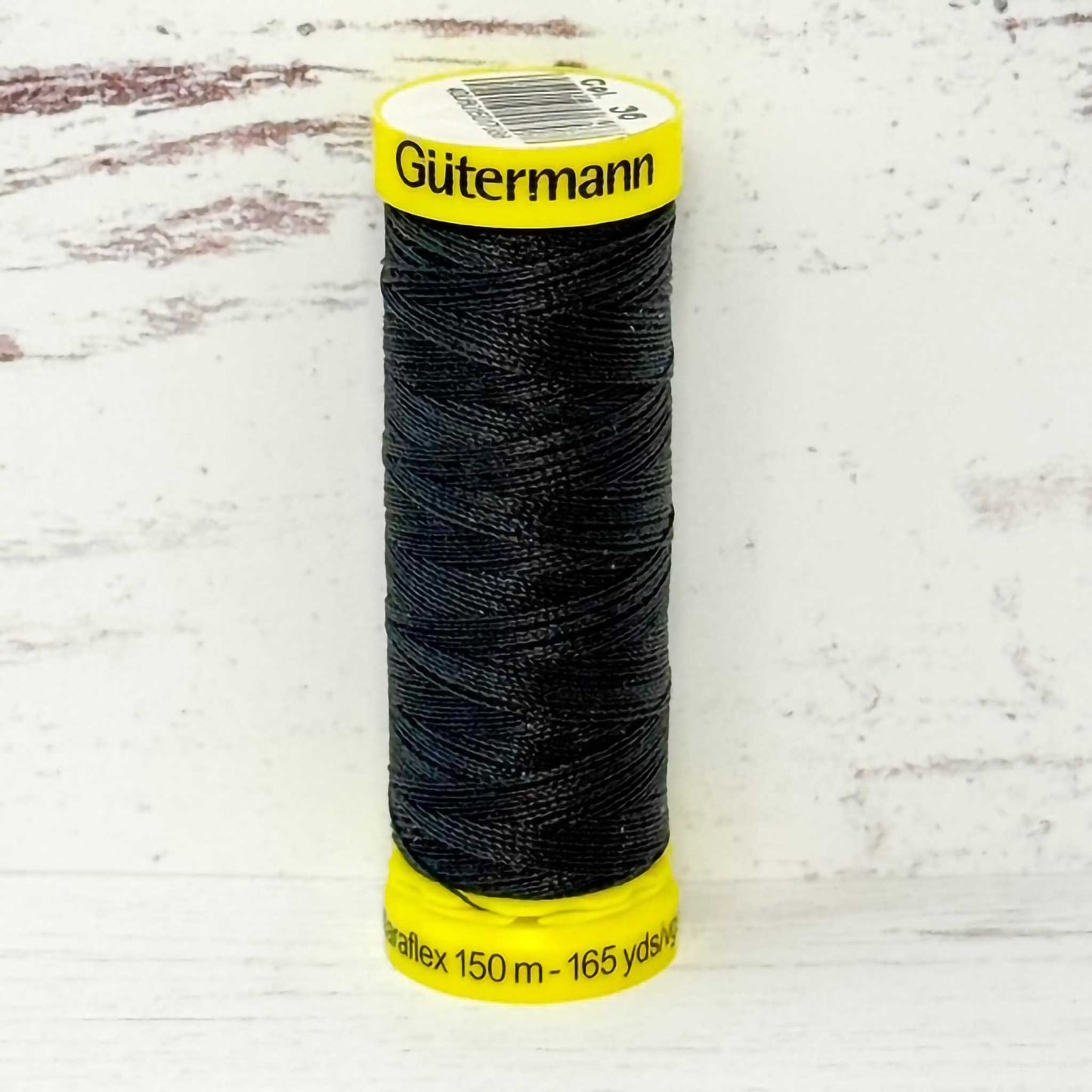 Spool of charcoal Gutermann thread on a light wooden surface