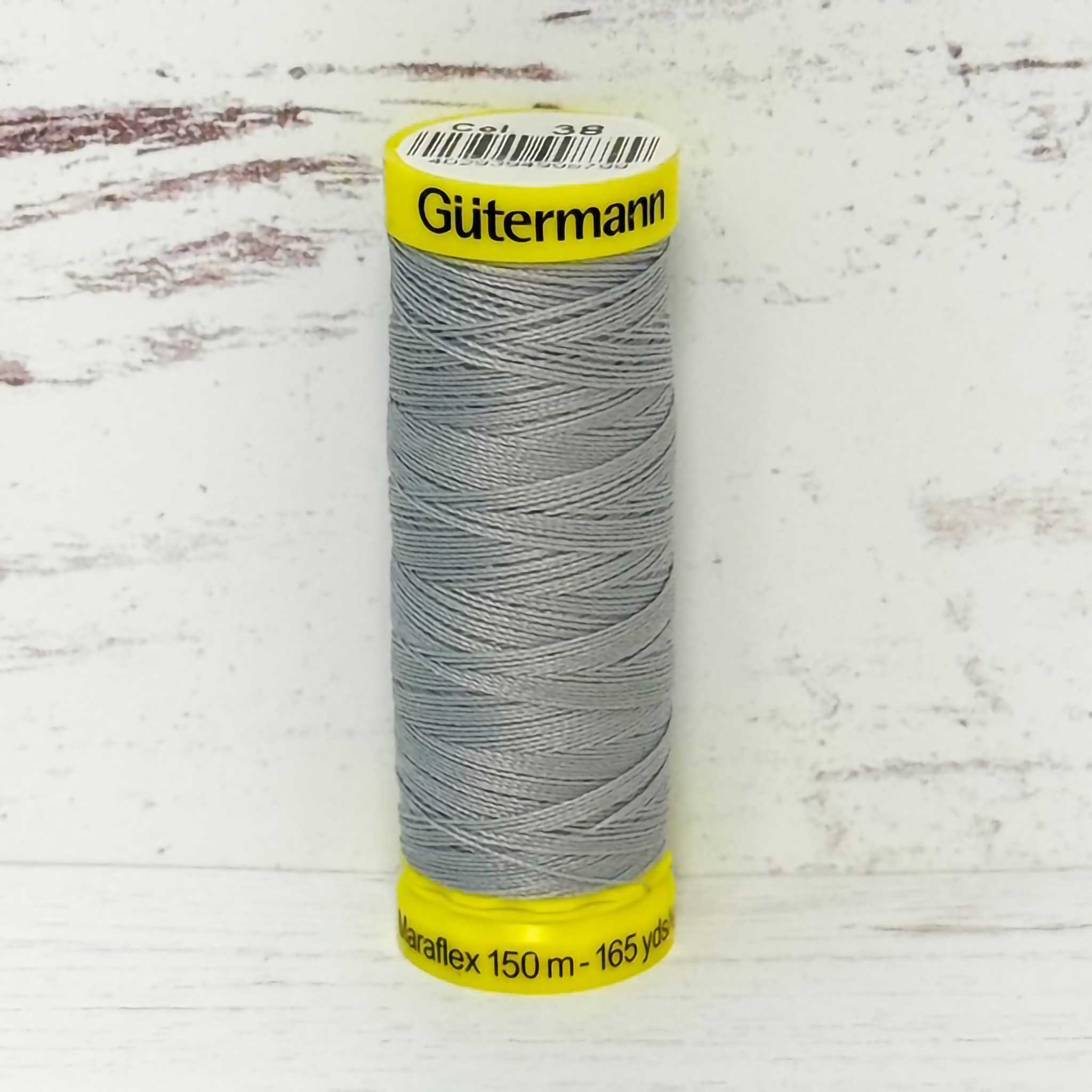 Spool of silver Gutermann thread on a textured white background