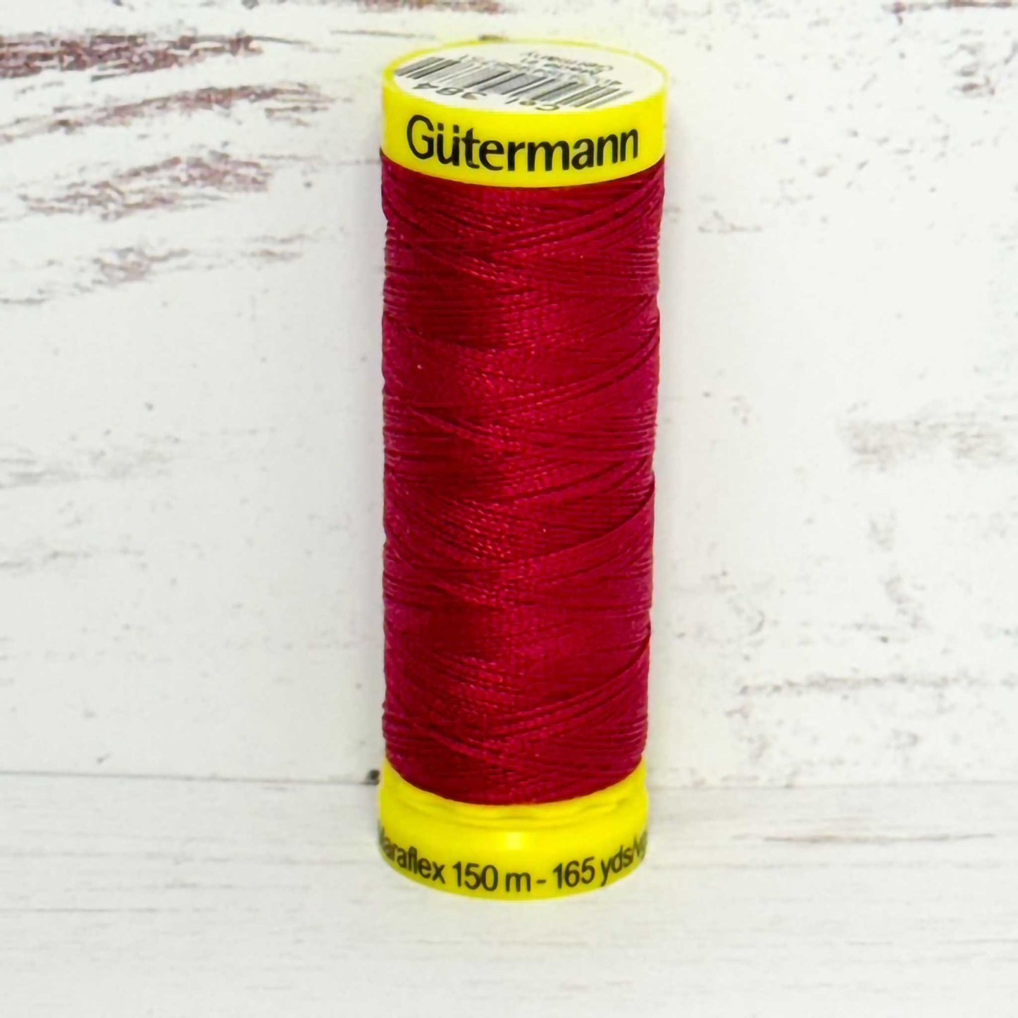Spool of red Gutermann thread on a light wooden surface
