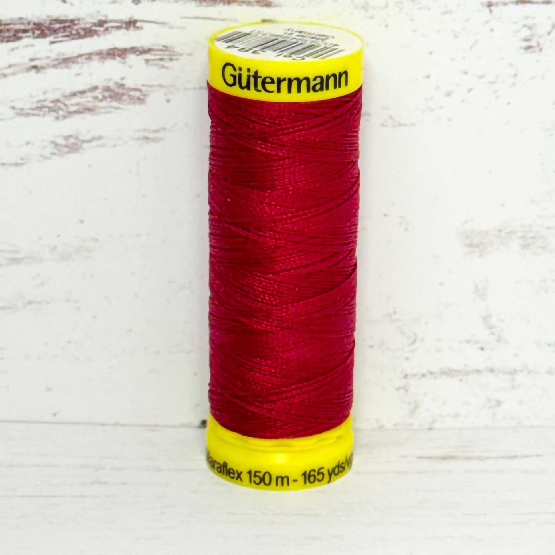 Spool of red Gutermann thread on a light wooden surface