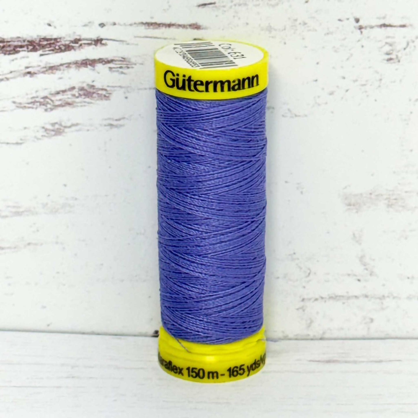 Spool of lilac thread with yellow label on a white wooden surface