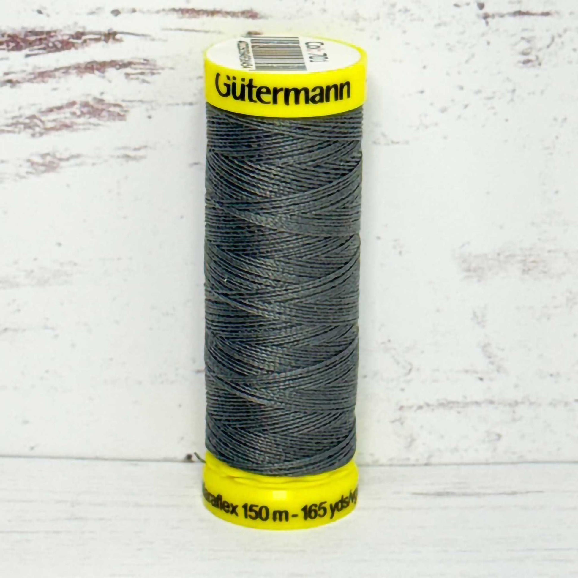 Spool of gray Gutermann thread on a light wooden surface
