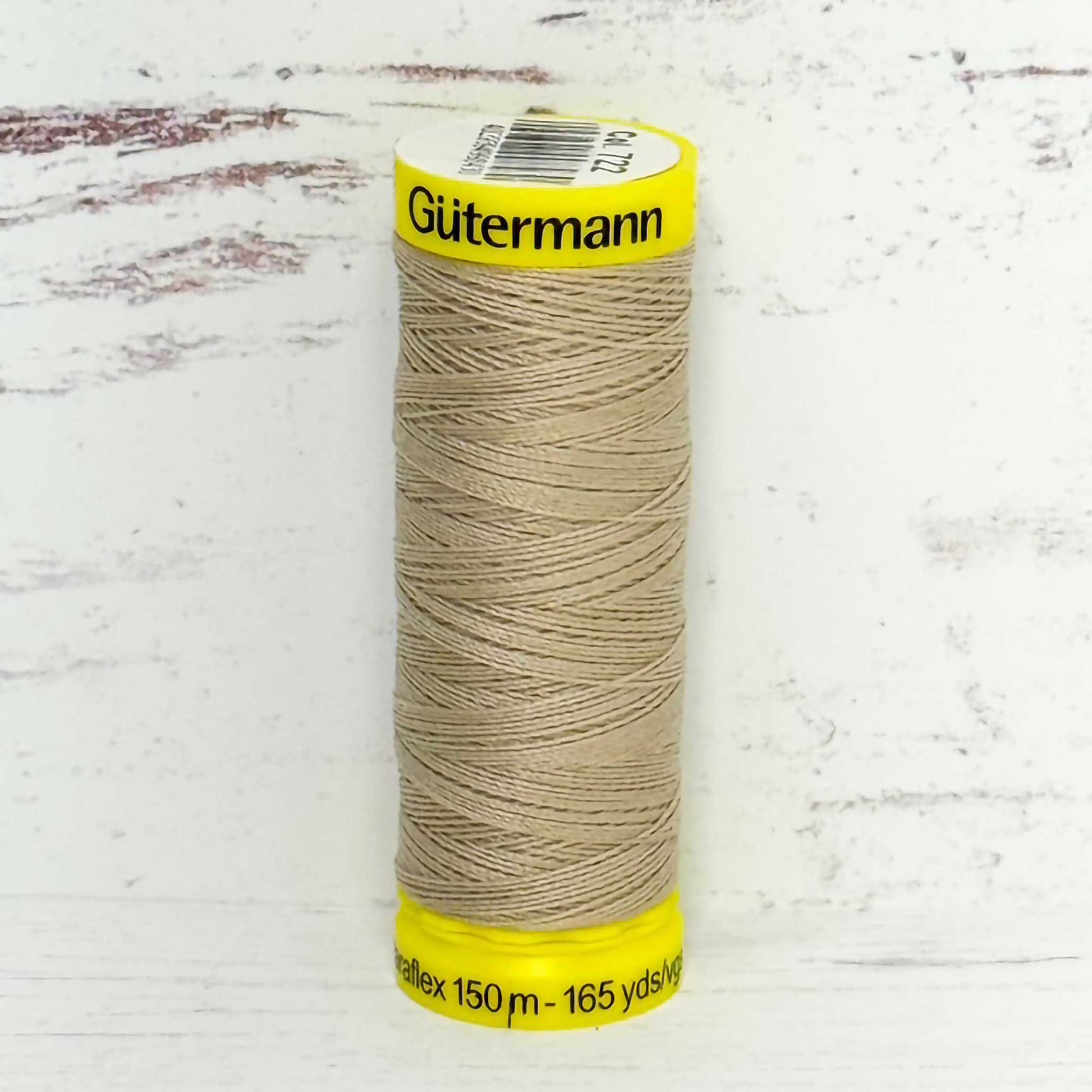 Spool of beige Gütermann thread on a textured white background