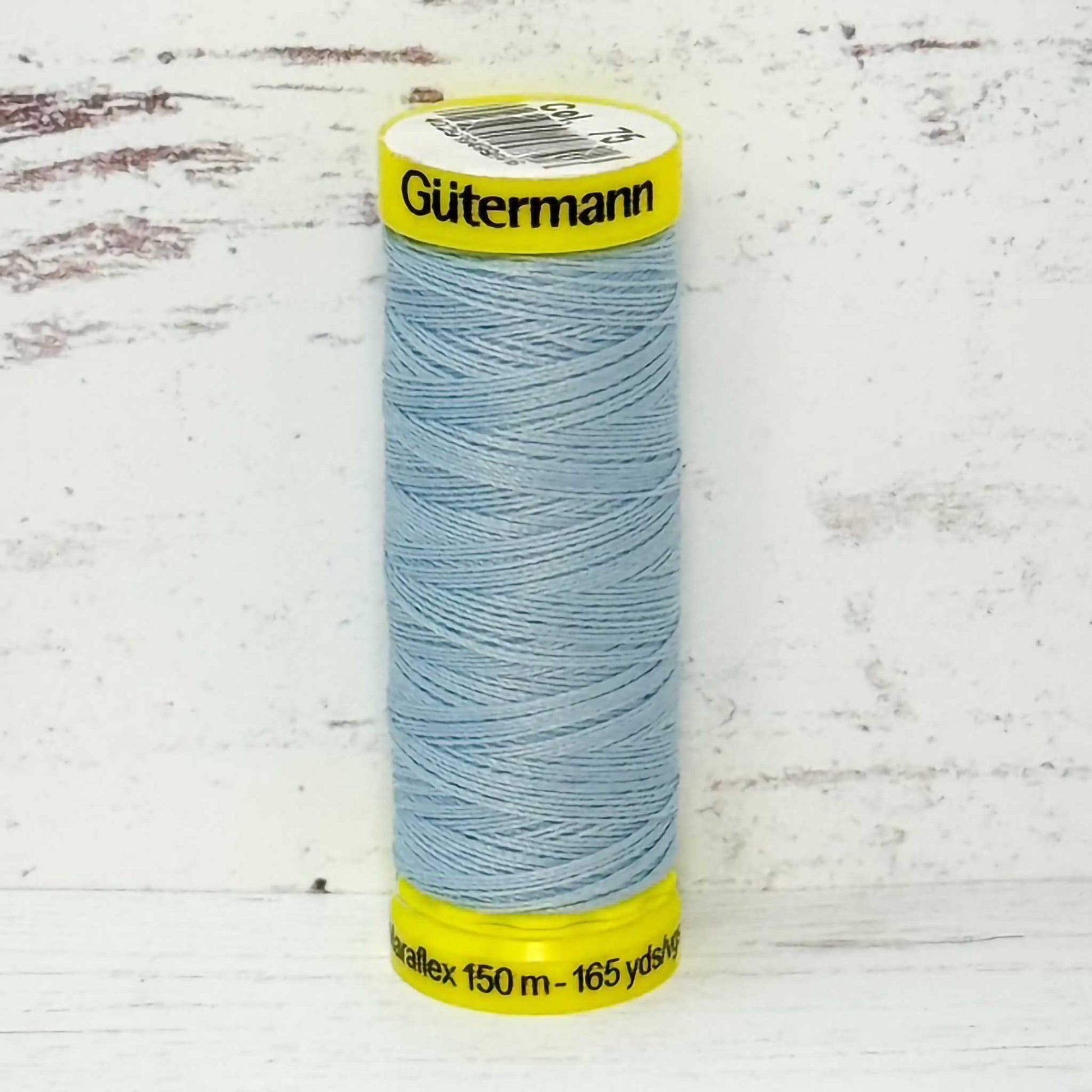 Spool of light blue Gutermann thread on a textured white background