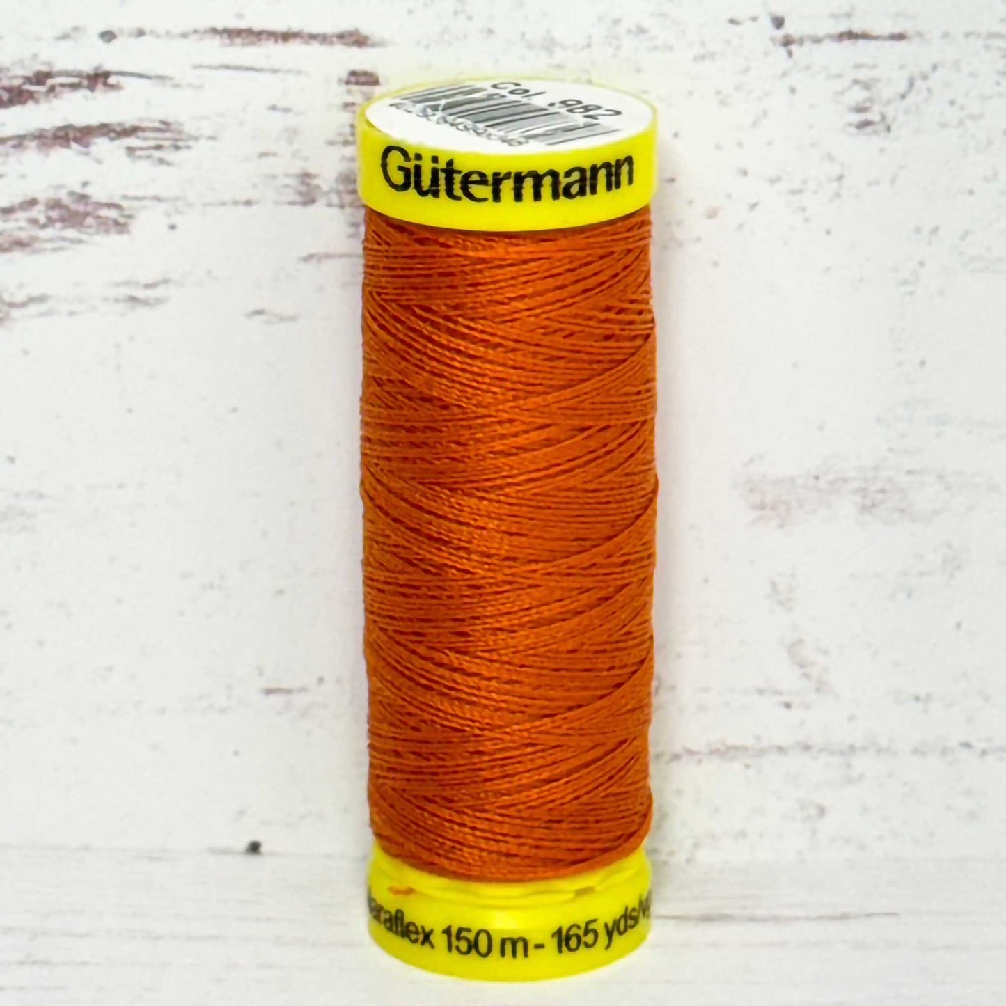 Spool of orange thread with yellow label on a light wooden surface