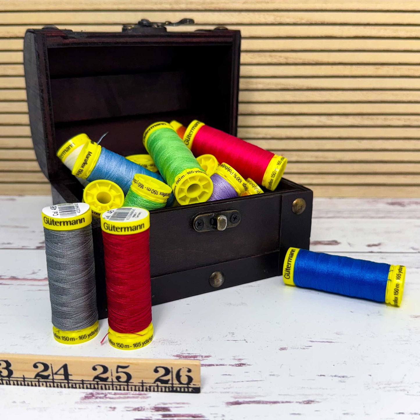 Colorful spools of thread in an open black toolbox on a wooden surface with a ruler.