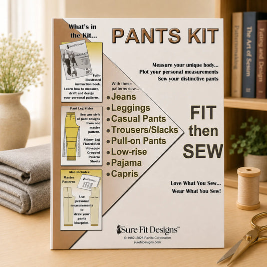 A 'Pants Kit' by Sure Fit Designs by Lori Fitzgerald is displayed on a wooden table in a styled home environment with a sewing book, thread spool, and scissors. The kit packaging features a white and tan design with illustrations of different pant styles.