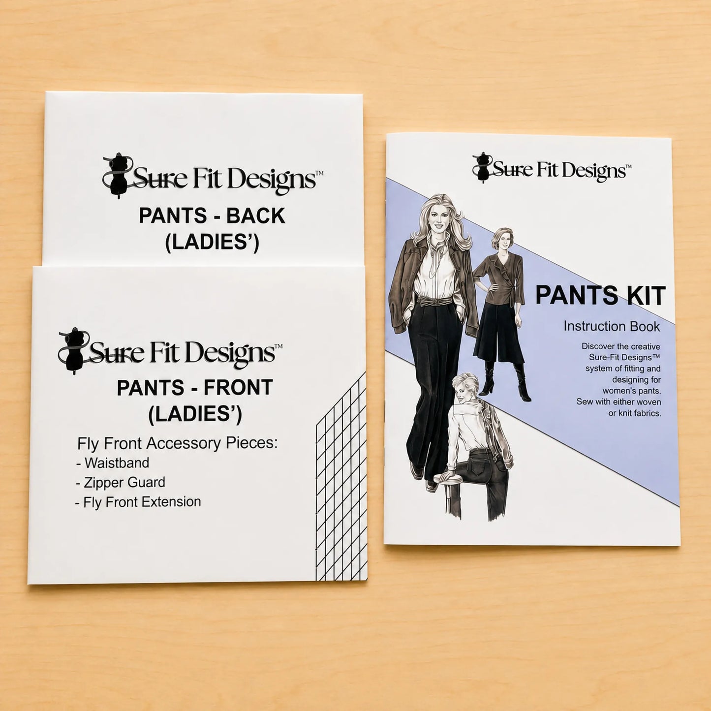 Three Sure Fit Designs paper packaging cards for a pants kit laid out on a light wood surface: two white cards labeled pants back and front for ladies, and one card labeled instruction book for the pants kit.