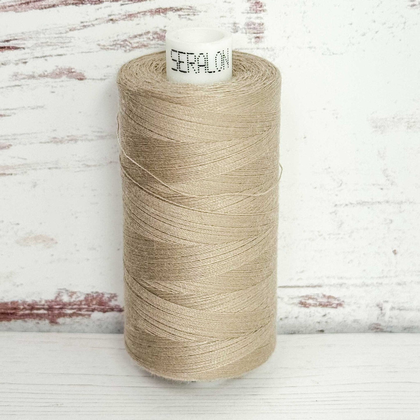 Spool of beige thread with 'Seralon' label on a wooden background