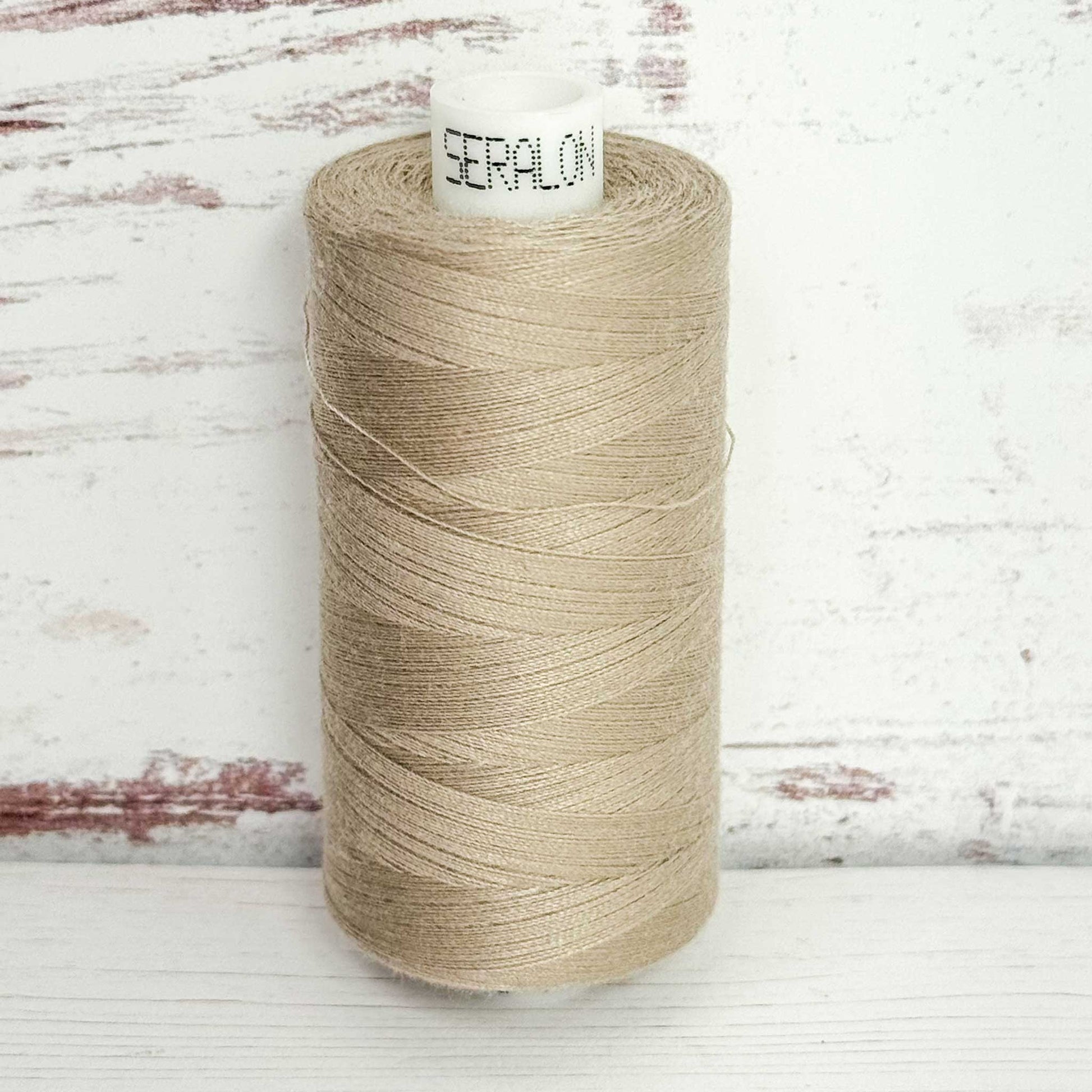 Spool of beige thread with 'Seralon' label on a wooden background