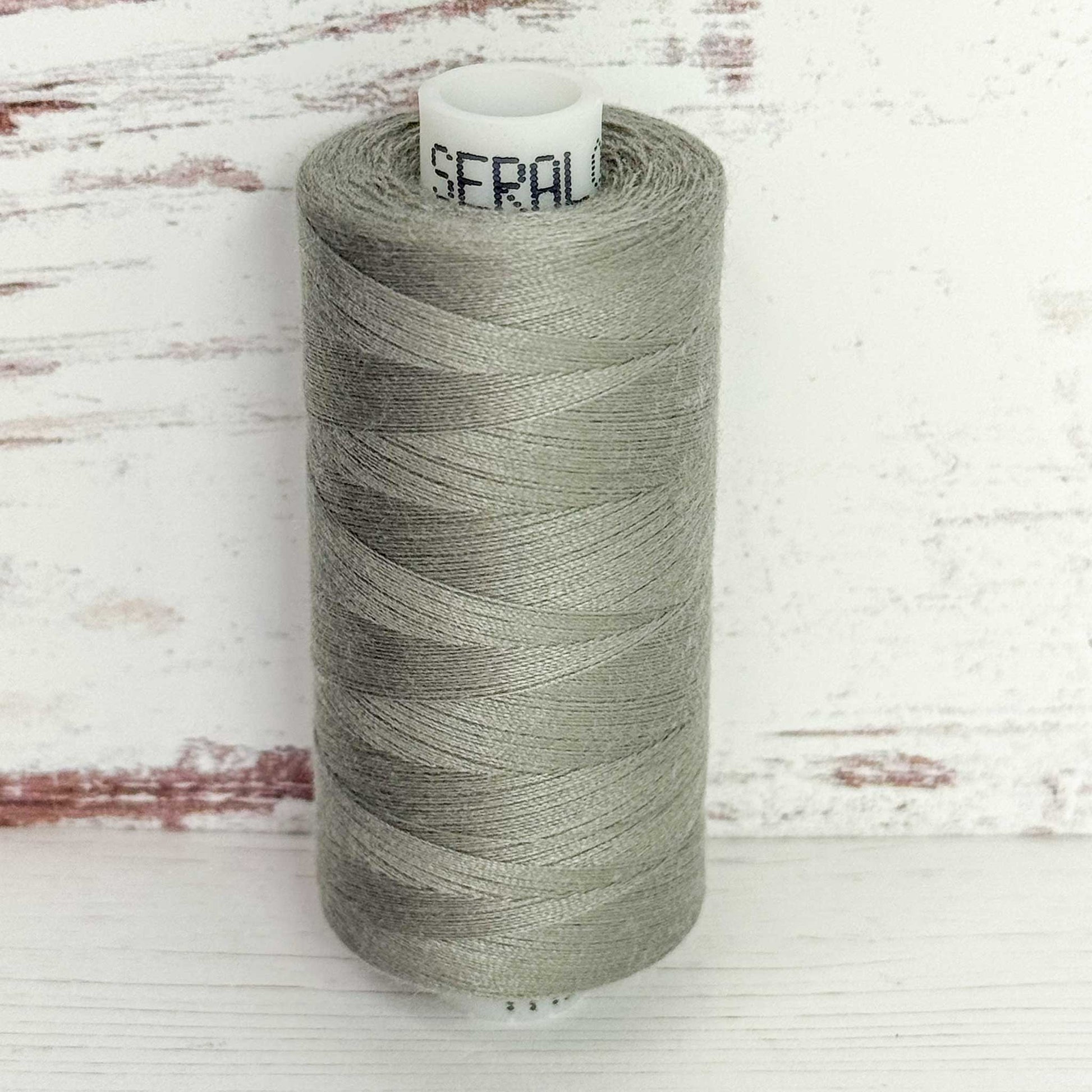 Spool of gray thread with 'Seral' label on a wooden background